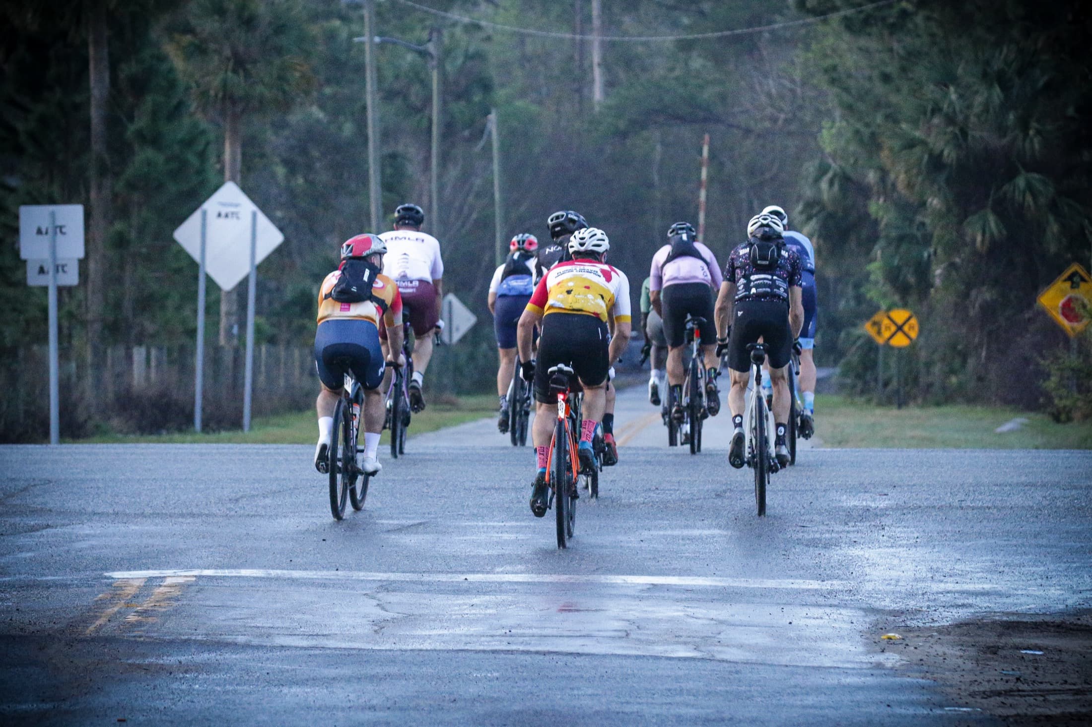 A group of riders rolling away down a wet road at dusk