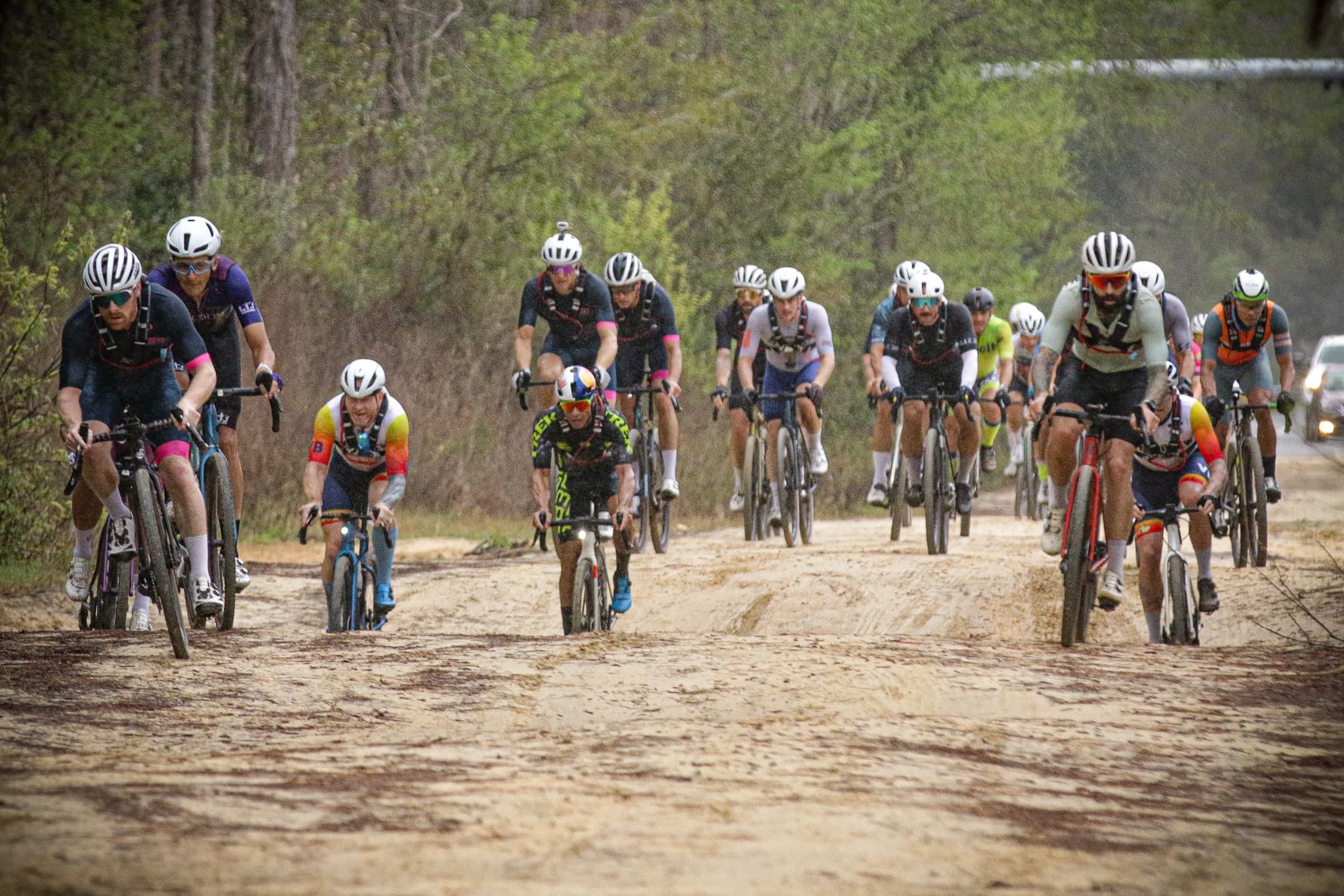 A gravel race group spread across a sandy road, riding toward the camera