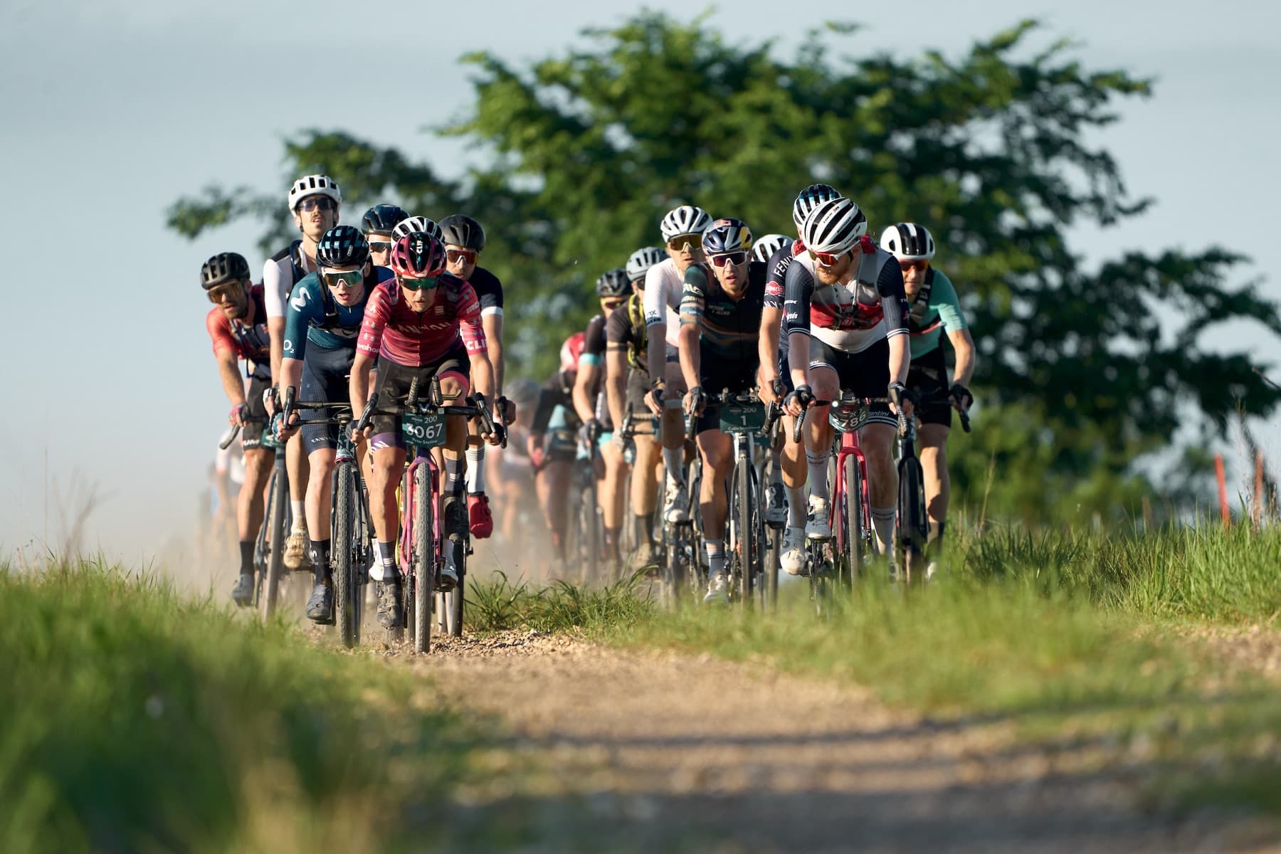 The lead group of the Unbound 200 riding a gravel road through the Flint Hills at dawn, dust rising behind them